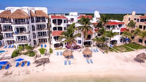 A resort with multiple buildings, a beach with sun loungers and umbrellas, and palm trees. - Steps to the sea! Charming garden view studio with beach access, WiFi and AC. (Akumal)