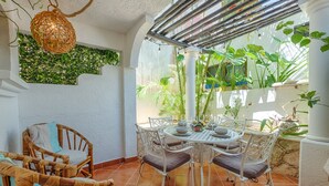 A dining area with a round table, white chairs, and a hanging light fixture. - Steps to the sea! Charming garden view studio with beach access, WiFi and AC. (Akumal)