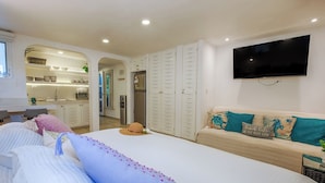 A bedroom with a bed, a TV, a sofa, and a kitchenette. - Steps to the sea! Charming garden view studio with beach access, WiFi and AC. (Akumal)