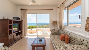 A living room with a television, a sofa, and a coffee table. There is a large window with a view of the ocean. - Oceanfront Akumal Villa With Pool Near Snorkeling & Restaurants (Akumal)