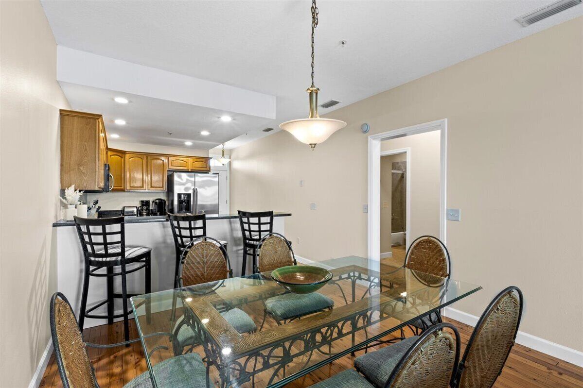 A modern kitchen with wooden cabinets, a glass dining table with chairs, and a hanging light fixture.