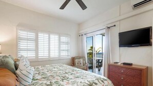 A bedroom with a bed, a dresser, a television, and a balcony with a view.