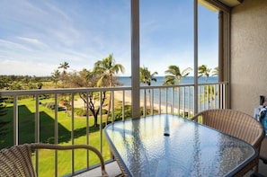 Ein Balkon mit Glastisch und Korbstühlen, der Blick auf einen Strand und Palmen freigibt.