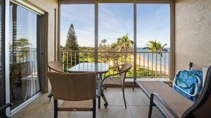 A balcony with a table and chairs, a view of the ocean, and a palm tree.