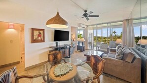 A spacious living room with a glass dining table, comfortable seating, a flat-screen TV, and a ceiling fan.
