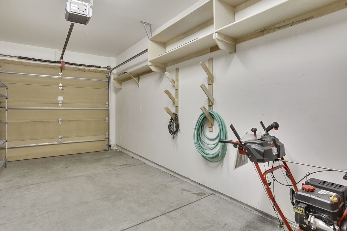 A garage with a closed garage door, a red lawnmower, and a green hose on the wall.