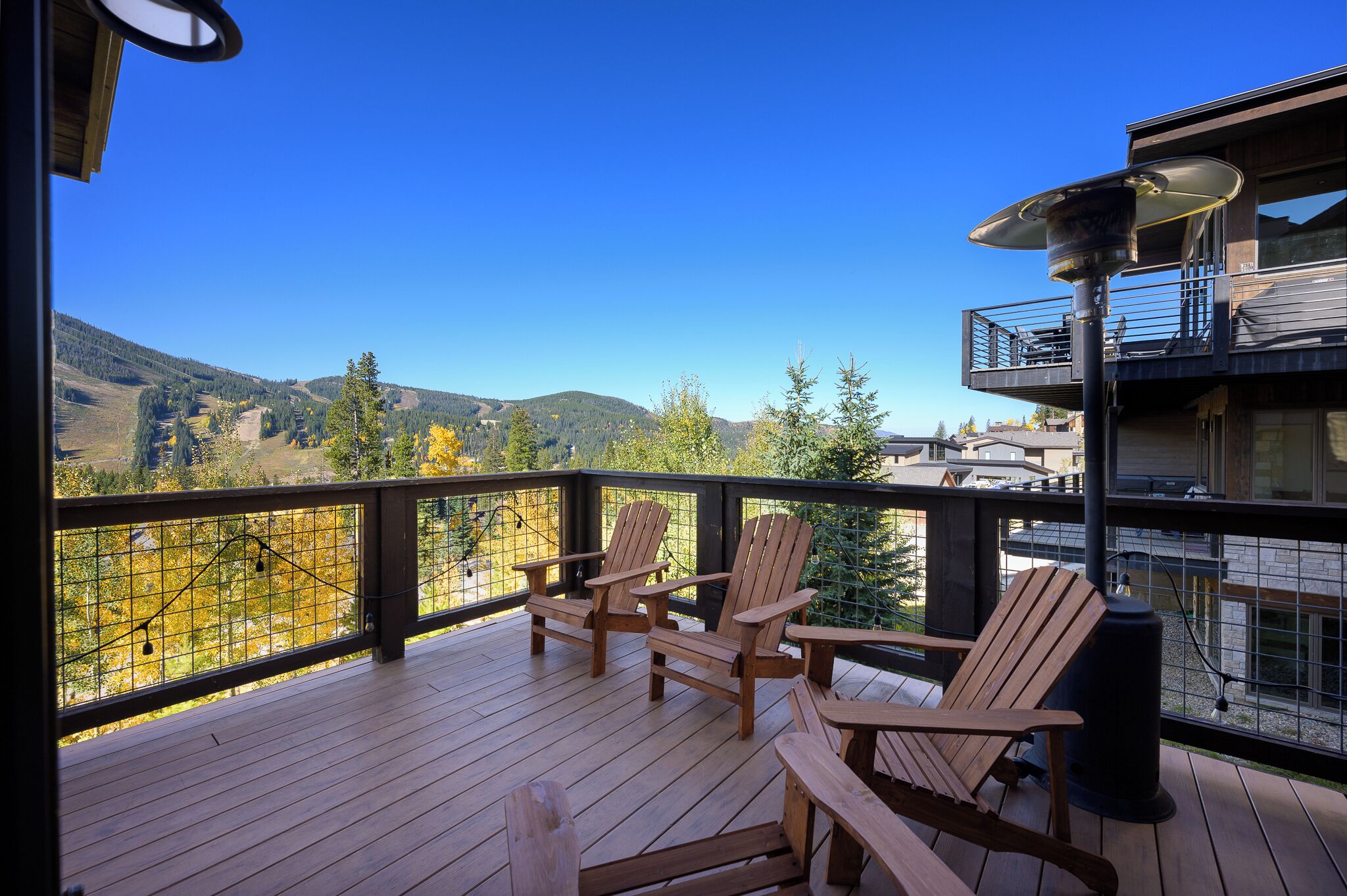 A wooden deck with Adirondack chairs and a view of a mountainous landscape.