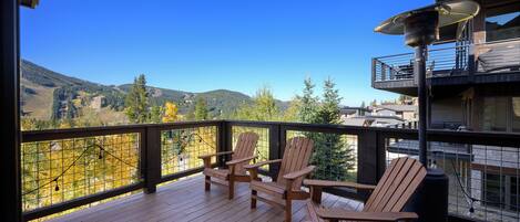 A wooden deck with Adirondack chairs and a view of a mountainous landscape.