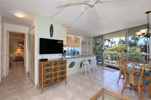 A kitchen with a TV, wooden cabinet, and bar stools. - Exceptional Location, Breathtaking Ocean View: Kamaole Nalu #204 (Kihei, Maui)