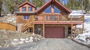 A log cabin with a stone foundation, a red garage door, and a balcony with a wooden railing. - Free SkyCard Activities - Ski Area Views, Private Hot Tub - Barton Cabin (Breckenridge)