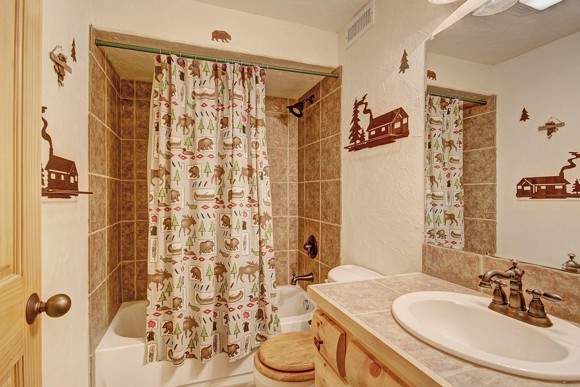 A bathroom with a shower curtain featuring animal prints, a toilet, a sink with a mirror, and a wooden cabinet.