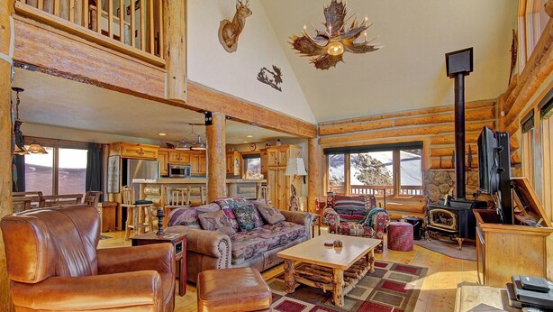 A spacious living room with a fireplace, leather furniture, and a large window overlooking a snowy landscape. - Free SkyCard Activities - Ski Area Views, Private Hot Tub - Barton Cabin (Breckenridge)
