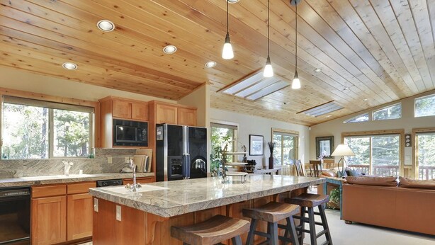 Une cuisine spacieuse avec des meubles en bois, un grand îlot central doté de tabourets et un coin repas avec un canapé.