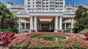 A multi-story hotel with a central entrance, a fountain, and a garden with pink flowers. - Poolside Condo w/ GOLF CART! Tram to Beach. Steps to Pool and Baytowne Wharf! (Miramar Beach)