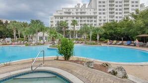 A swimming pool with lounge chairs and palm trees, surrounded by a building with balconies. - Poolside Condo w/ GOLF CART! Tram to Beach. Steps to Pool and Baytowne Wharf! (Miramar Beach)