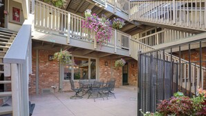 Un espace patio avec un bâtiment en briques, du mobilier d’extérieur et des jardinières suspendues.