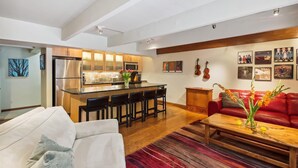 Un salon moderne avec un canapé rouge, un divan blanc et une table basse en bois. Il y a également un coin cuisine avec un bar et un réfrigérateur.