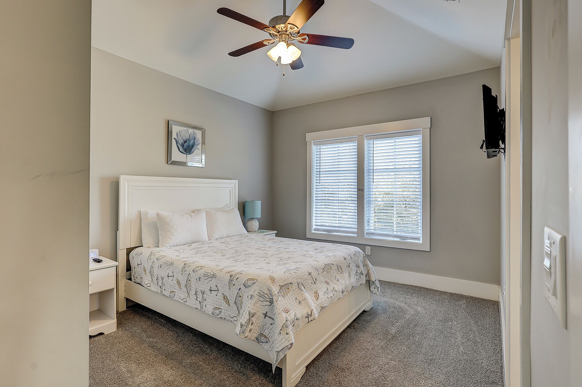 A bedroom with a bed, a nightstand, a ceiling fan, and a window with blinds.