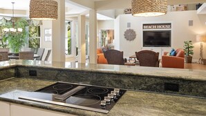 Une cuisine moderne dotée d’une cuisinière intégrée, un coin repas avec des chaises en osier et un salon avec un téléviseur et des éléments de décoration murale.