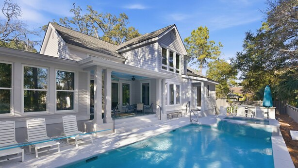 Une maison avec une piscine, une façade blanche et un patio couvert avec des chaises.