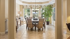 Un coin repas avec une table ronde, des chaises en osier, un lustre et une plante en pot.