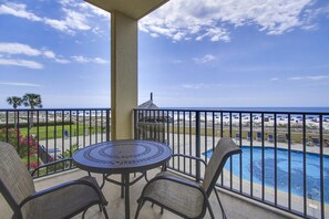 Un balcon avec vue sur la plage et l’océan. On y trouve une table ronde avec des chaises et une petite piscine.
