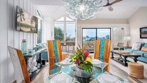 A dining area with a glass table set for four, a large painting on the wall, and a view of the outdoors.