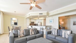A living room with two grey sofas, a ceiling fan, and a kitchen in the background. - Updated Beachfront Condo w/ Great Views From Private Balcony in Destin! 🌊🌴🐬 (Destin)