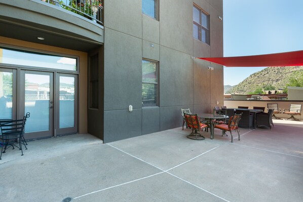 An outdoor patio with a table and chairs, a red umbrella, and a view of a mountain in the background.