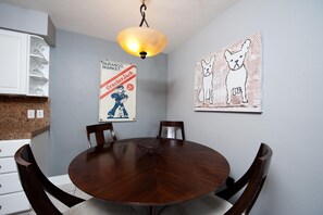 Comedor con una mesa redonda de madera, cuatro sillas, una lámpara colgante y dos obras de arte en la pared que representan perros.