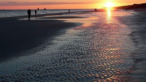 Ein Strand bei Sonnenuntergang, Menschen spazieren am Ufer entlang.