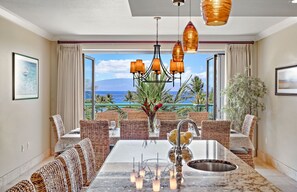 Enjoy meals in this dining area with a large table and wicker chairs, surrounded by ocean views and palm trees.