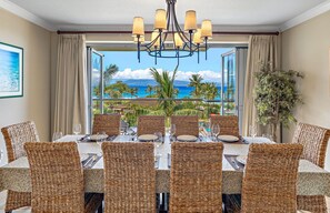 A dining area with wicker chairs, a chandelier, and a view of the ocean.