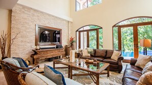 A spacious living room with a stone wall, leather sofas, a glass coffee table, and a large TV. - Luxury Home, Casa Vista Paraíso, Pool, Rainforest View, Access to Amenities. (Puntarenas)