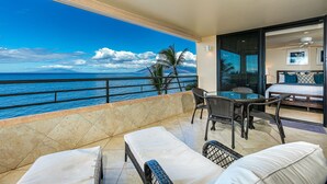 Un balcone con vista sull'oceano, un'area pranzo con mobili in vimini e una camera da letto con un letto e un comodino.