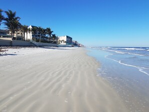 A beach with a sandy shore, palm trees, and buildings in the background.