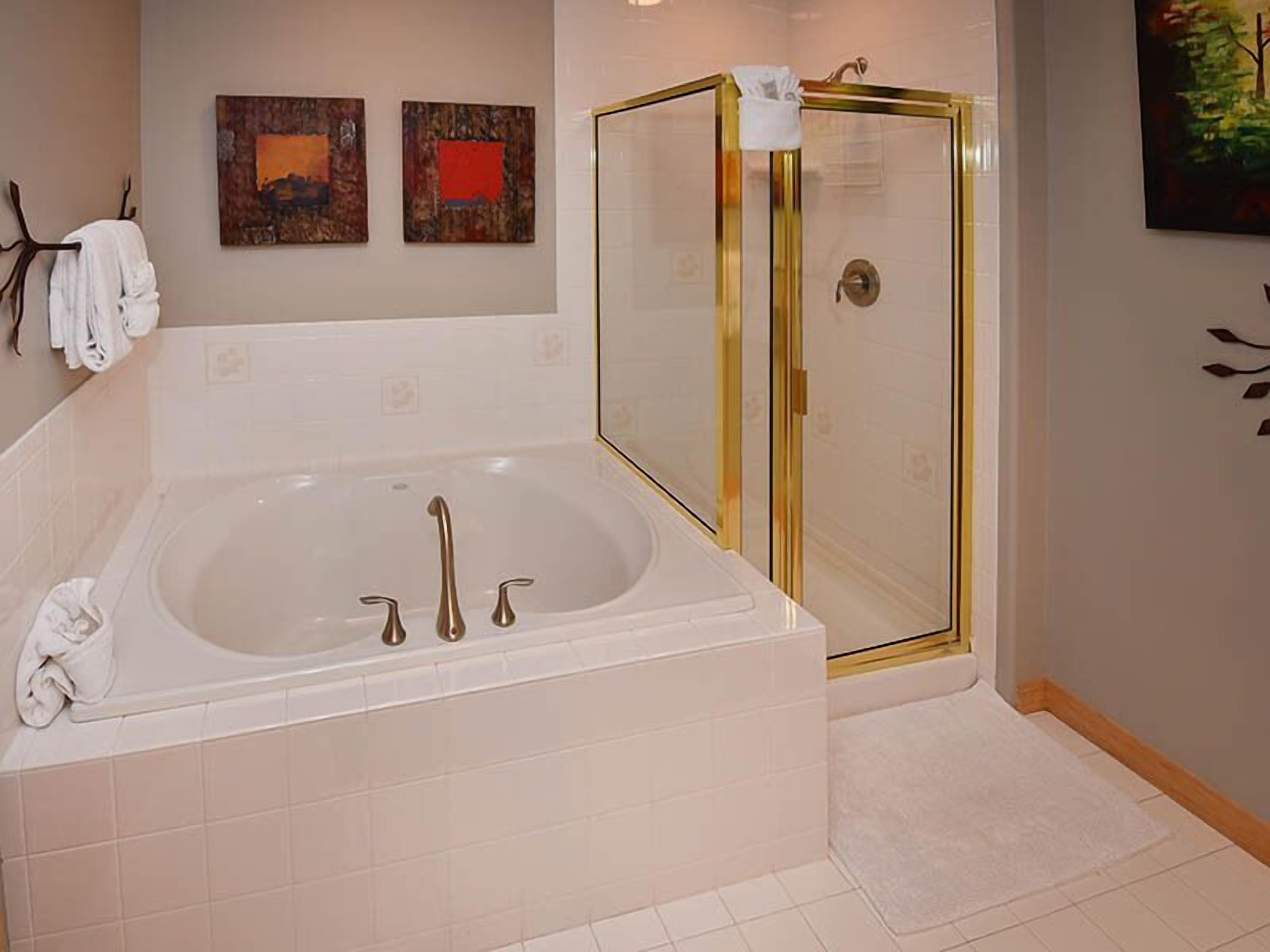 A bathroom with a large bathtub, a glass shower enclosure, and two wall-mounted artwork pieces.