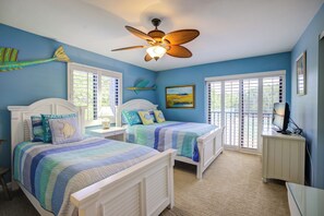 Une chambre avec deux lits, un ventilateur de plafond et de grandes fenêtres.
