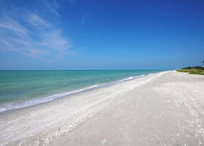 Une vaste plage de sable fin, avec des vagues douces et un ciel bleu dégagé.