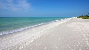 A wide, sandy beach with gentle waves and a clear blue sky.