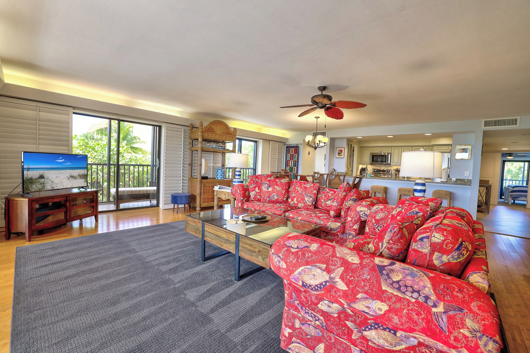 A spacious living room with a large red sofa, a glass coffee table, and a television displaying a beach scene.