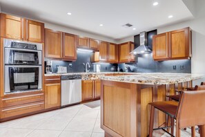 A modern kitchen with wooden cabinets, stainless steel appliances, and a marble countertop.