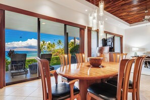 A dining area with a large table and chairs, a wooden ceiling, and a view of the ocean.
