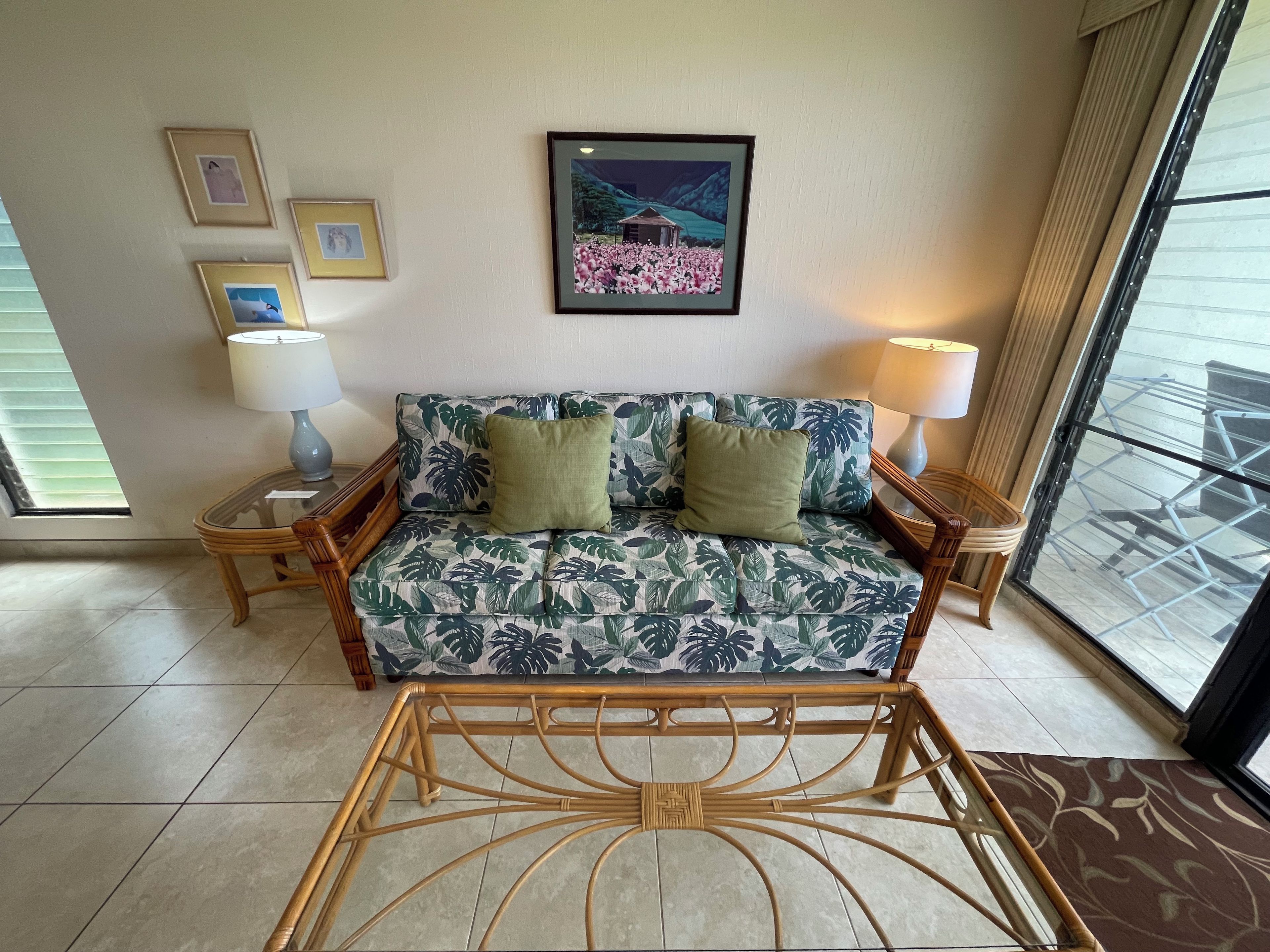 A room with a sofa, two lamps, framed pictures on the wall, and a window with a view.