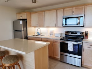 A modern kitchen with wooden cabinets, a stainless steel refrigerator, a microwave, a stove, and a sink.