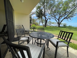 A patio with a round table and chairs, a small garden, and a view of the ocean.