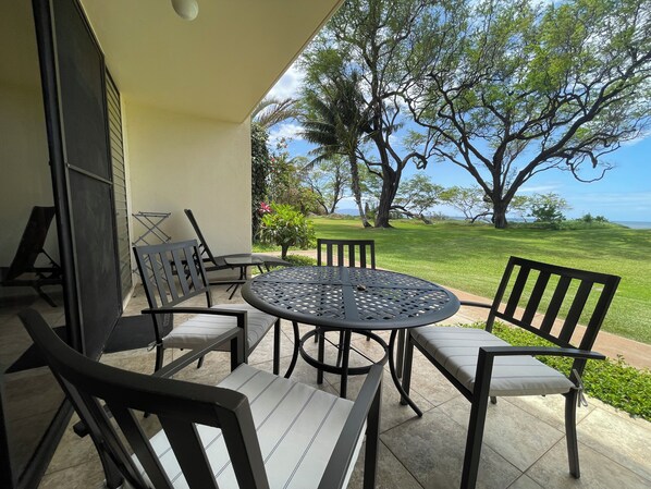 Une terrasse avec une table ronde et des chaises, un petit jardin et une vue sur l’océan.