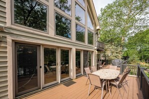 A deck with a table and chairs, large sliding glass doors, and a view of the surrounding trees. - Magical Lake Escape w/ Dock Slip & Game Room (Oakland)