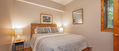 A bedroom with a wooden bed, bedside lamps, a framed picture on the wall, and a window with blinds.