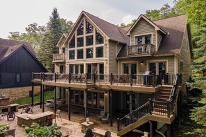 A two-story house with a balcony, outdoor seating area, and a stone fireplace. - Magical Lake Escape w/ Dock Slip & Game Room (Oakland)